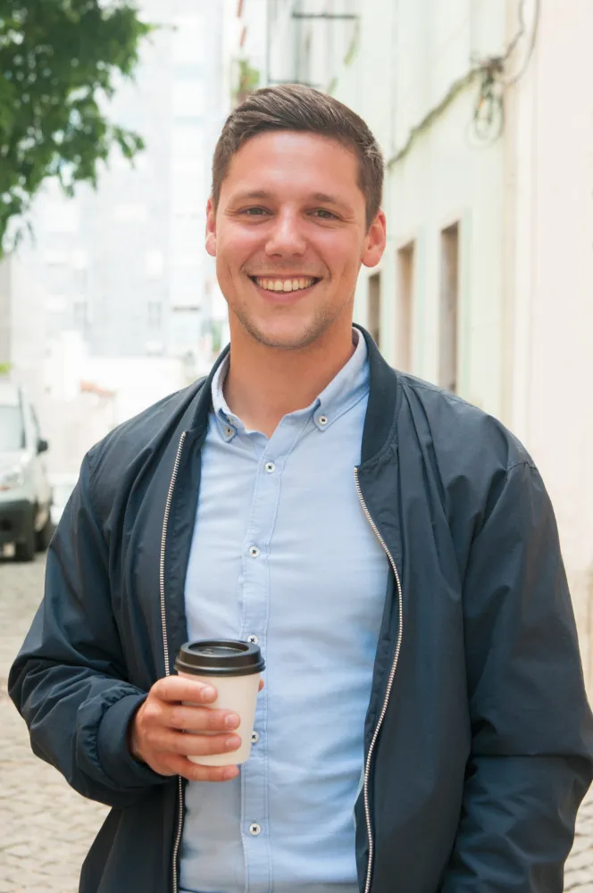 A man wearing a blue shirt and jacket is holding a cup of coffee.